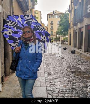 Dame souriante avec un parapluie bleu ouvert dans une rue de Gérone. Il pleut Banque D'Images