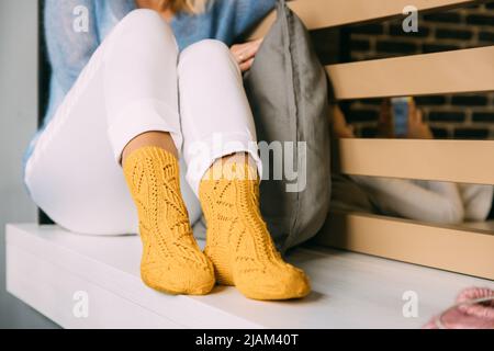 Confortable femme confortable en laine tricotée jaune hiver chaussettes, pantalon blanc et chandail chaud bleu reposant sur un banc au café en hiver Banque D'Images