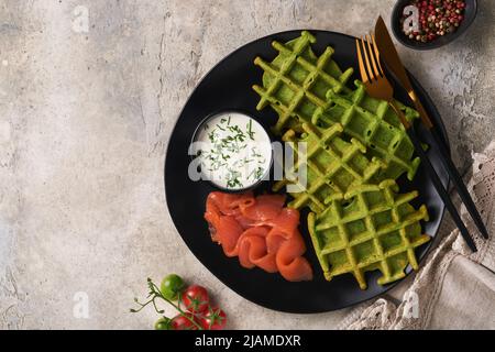 Gaufres belges vertes. Épinards ou ail sauvage ou gaufres au pesto avec saumon rouge et sauce à la crème sur fond de table en béton gris. Délicieux petit déjeuner, Banque D'Images