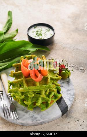 Gaufres belges vertes. Épinards ou ail sauvage ou gaufres au pesto avec saumon rouge et sauce à la crème sur fond de table en béton gris. Délicieux petit déjeuner, Banque D'Images