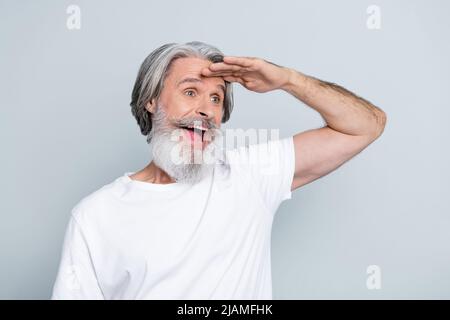 Photo d'impressionné drôle retraité homme porter t-shirt blanc tête de bras regardant loin vide espace isolé couleur gris fond. Banque D'Images