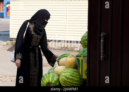Une femme musulmane vêtue de vêtements nationaux inspecte le marché de la ville de pastèques et de melons. Banque D'Images
