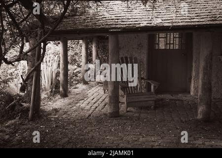 Image intemporelle, nostalgique, de la vieille pierre, hangar en pots aux piliers avec plancher pavé, vieux sièges en bois et wisteria à Trewithen Cornwall Banque D'Images