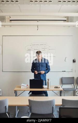 Professeur de sexe masculin regardant un ordinateur portable sur le bureau dans une salle de classe Banque D'Images