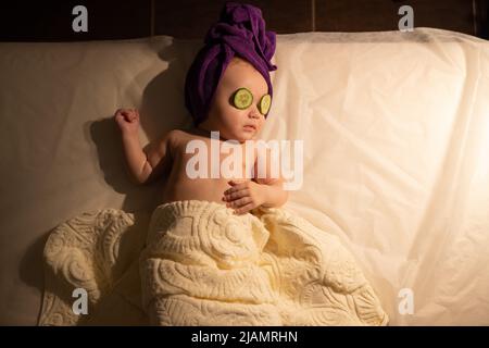 Petite fille bébé bébé bébé enfant allongé sur les yeux de concombre de lit. Banque D'Images