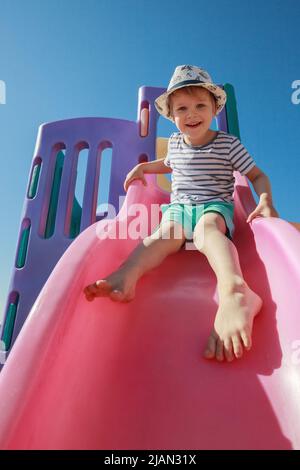 Enfant souriant jouant sur la barre coulissante jouet aire de jeux en plein air, heureux petit enfant d'âge préscolaire ayant drôle tout en jouant sur l'équipement de jeu dans le d Banque D'Images
