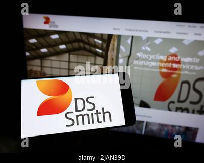 Personne tenant un téléphone portable avec le logo de la société britannique d'emballage DS Smith plc à l'écran en face de la page Web de l'entreprise. Mise au point sur l'affichage du téléphone. Banque D'Images