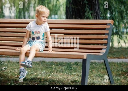 Petit garçon dans le parc de la ville d'été assis sur un banc. Banque D'Images