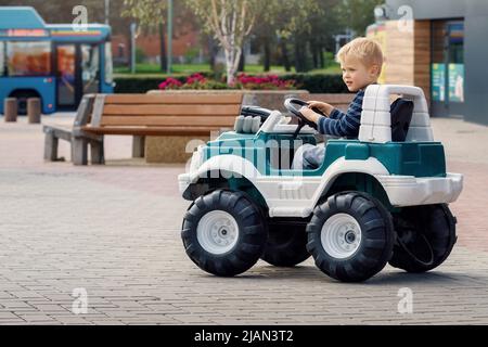 Petit garçon d'enfant d'âge préscolaire qui conduit une grande voiture de jouet et s'amuser à l'extérieur. Enfant bénéficiant d'une chaude journée d'été dans le paysage de la ville. Banque D'Images