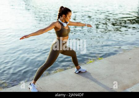 Jolie jeune femme en vêtements de sport s'étendant sur une promenade de rivière Banque D'Images