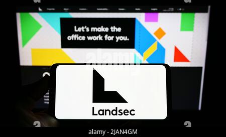 Personne tenant un téléphone portable avec le logo de la société Land Securities Group plc (Landsec) sur l'écran en face de la page Web de l'entreprise. Mise au point sur l'affichage du téléphone. Banque D'Images