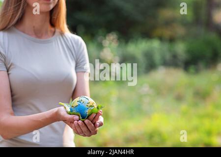 Jeune femme tenant une petite planète entre les mains contre le fond vert du printemps ou de l'été. Écologie, environnement et concept du jour de la Terre. Éléments de ceci Banque D'Images