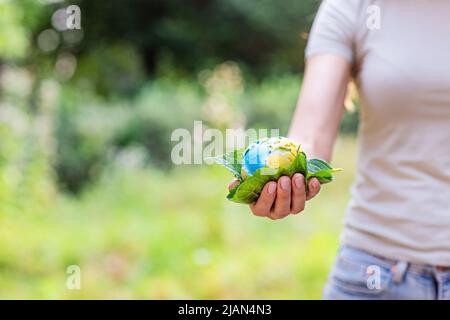 Jeune femme tenant une petite planète entre les mains contre le fond vert du printemps ou de l'été. Écologie, environnement et concept du jour de la Terre. Éléments de ceci Banque D'Images