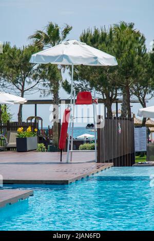 Siège vide du maître-nageur près de la piscine. Chaise rouge sous un parasol blanc sur une tour au bord de la piscine Banque D'Images