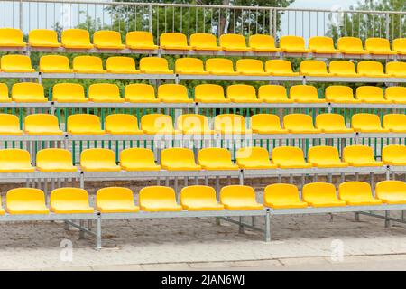 Vide statifs de stade vacants, chaises, plastique jaune aréna sièges de spectateur sur un petit terrain de football, jour, PAN, personne. Pas de personne, sport ev Banque D'Images