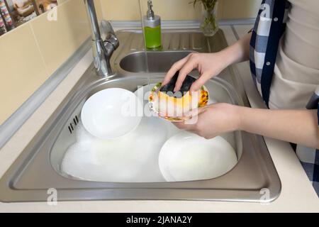 La fille lave beaucoup de vaisselle sale dans l'évier de cuisine. Banque D'Images