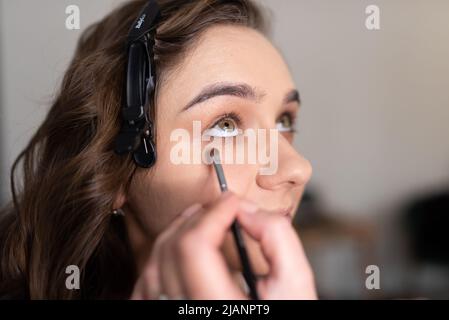 Maquilleuse application de l'ombre oculaire à la paupière inférieure d'une fille avec un pinceau. Photo de haute qualité Banque D'Images