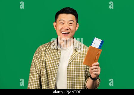 Concept de billets bon marché. Homme asiatique d'âge moyen heureux, détenteur d'une carte d'embarquement et d'un passeport, debout sur fond vert Banque D'Images