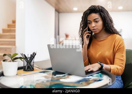 Jeune femme noire travaillant et parlant au téléphone à la maison Banque D'Images