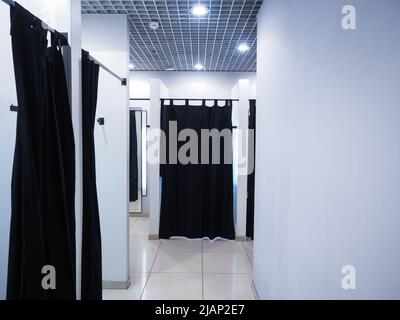 Cabine d'essayage lumineuse avec murs blancs et rideaux noirs sur les cabines. Magasin de vêtements. Banque D'Images