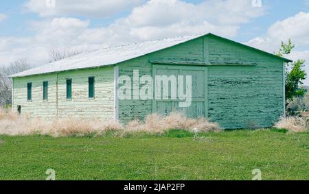 Un bâtiment de service ferme robuste avec une ancienne porte de garage coulissante dispose de trois pièces intérieures pour le stockage et le travail sur l'équipement. La peinture verte est usée. Banque D'Images