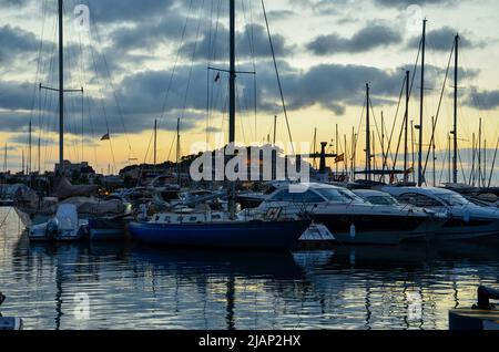 Yachts et voiliers dans le port de Denia sous un ciel légèrement nuageux et coloré en soirée d'été avec le château de la montagne et le château de Denia en arrière-plan Banque D'Images