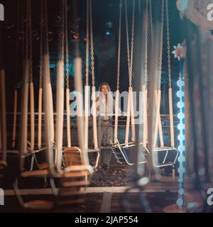 Une femme se tient au loin en regardant un carrousel lumineux vide dans un parc d'attractions nocturne. Mise au point douce. Banque D'Images