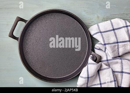 Vider la poêle ronde en fonte, le torchon sur une table en bois bleu clair. Modèle pour la mise en place des plats Banque D'Images