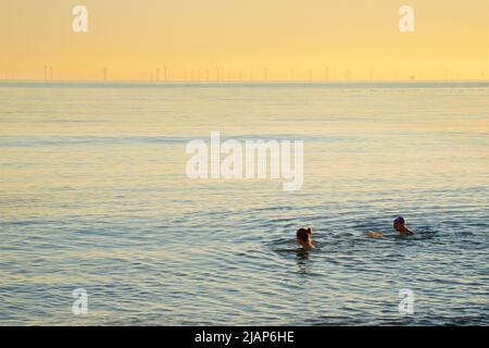 En hiver, nagez dans le canal anglais de Brighton. Deux femmes nageant. Brighton, East Sussex, Angleterre, Royaume-Uni. Parc éolien de Rampion à l'horizon. Banque D'Images