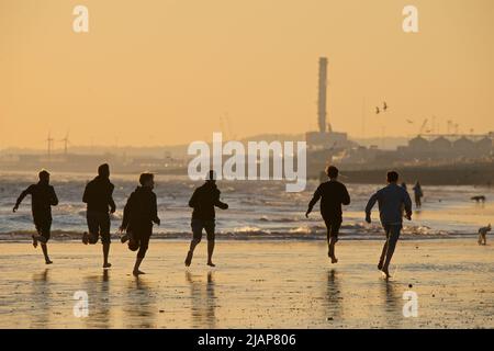 Silhoueted formes de personnes sur la plage à marée basse, Brighton & Hove, East Sussex, Angleterre, Royaume-Uni. Un groupe d'adolescents qui coulent pieds nus. Banque D'Images