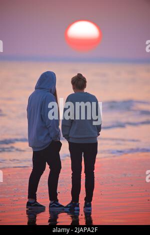 Un couple marchant ensemble sur la plage à marée basse, Sunset, Brighton, Angleterre, Royaume-Uni. Banque D'Images