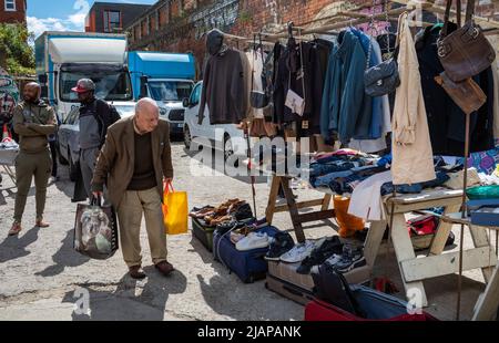 Un homme âgé passe devant une cabine de vêtements de seconde main au marché de Brick Lane à l'est de Londres, au Royaume-Uni Banque D'Images