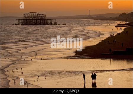 Silhoueted formes d'amis ensemble et d'autres personnes sur la plage à marée basse, Brighton & Hove, East Sussex, Angleterre, Royaume-Uni. Photographié depuis le Palace Pier. Shoreham Power Station au loin. Banque D'Images