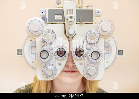 Un ophtalmologiste mâle vérifie la vue d'une jeune fille à l'aide d'un phoroptère. Traitement de la vision. Banque D'Images