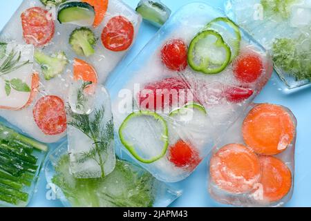 Légumes frais coupés congelés dans de la glace sur fond bleu Banque D'Images