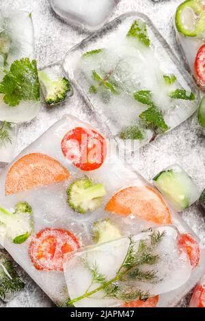 Légumes frais coupés congelés dans de la glace sur fond gris Banque D'Images