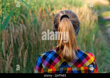 Refocalisation de la coiffure de queue de cheval. Jeune fille ou préadolescente marchant sur fond de nature et se tenant en arrière-plan. Petite fille d'enfant. Prairie verte. Génération z. Automne, Banque D'Images