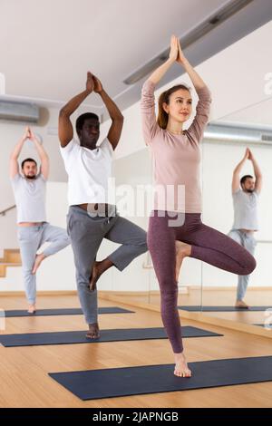 Groupe de personnes pratiquant la pose d'arbre dans la salle de gym Banque D'Images