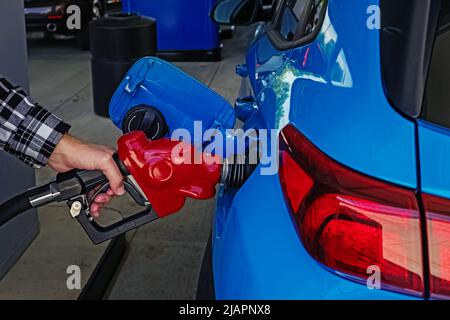 Main mâle tenant la pompe de remplissage d'essence dans la voiture, gros plan. Ravitaillement en voiture, prix de l'essence Banque D'Images