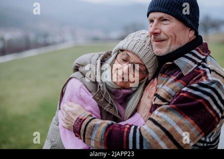 Homme âgé embrassant et consolant sa femme bouleversée à l'extérieur dans le jardin en hiver. Banque D'Images