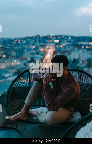 Portrait od déprimé jeune Africain - américain homme assis sur un balcon avec vue sur la ville en soirée. Banque D'Images