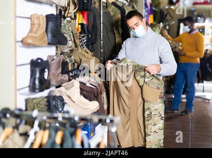 Homme en masque choisir des vêtements de camouflage Banque D'Images