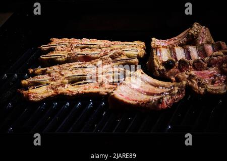 côte de bœuf juteuse et côte de porc lentement sur le gril au feu d'un barbecue à gaz Banque D'Images