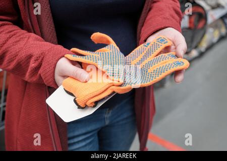 Une femme dans un magasin de matériaux de construction choisit pour acheter des gants avec des encoches en caoutchouc Banque D'Images