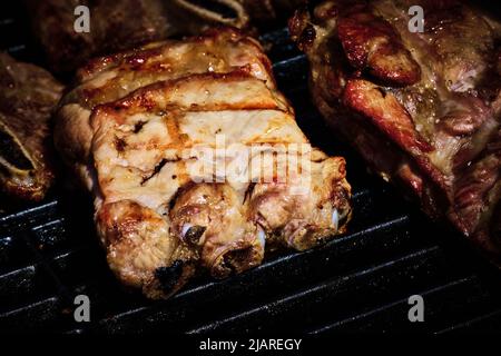 côte de bœuf juteuse et côte de porc lentement sur le gril au feu d'un barbecue à gaz Banque D'Images