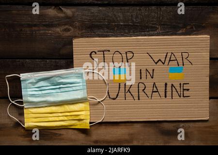 Les masques médicaux, jaunes et bleus, comme le drapeau de l'Ukraine, se trouvent sur une table en bois et un signe avec le texte arrête la guerre en Ukraine. Drapeau d'Etat d'Ukrain Banque D'Images