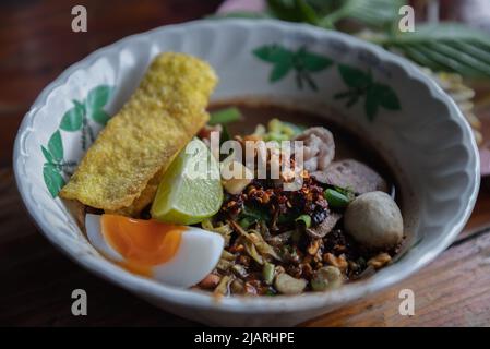 Nouilles jaunes aux œufs dans la soupe épaisse, ajout de sang avec des boules de porc, tranches de porc, tranches d'œufs de bael, tranches de citron vert et de wonton croustillant (nouilles aux œufs de Nam tok). TH Banque D'Images