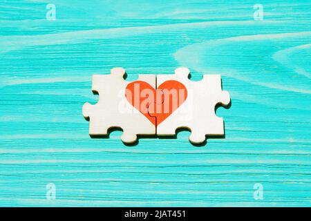 Symbole coeur fait de deux pièces de puzzle en bois sur fond bleu en bois. Concept d'âme correspondante. Banque D'Images