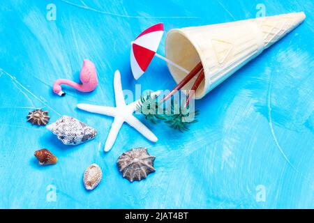 Cornet de gaufres à la crème glacée avec coquillages, palmiers, flamants roses et parasol sur fond bleu. Concept de forfait vacances d'été créatif. Banque D'Images