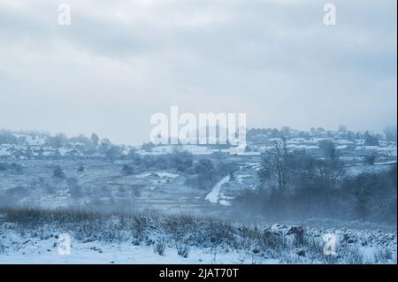 Vue sur le village de Llantrisant, au pays de Galles, après une lourde chute de neige d'une nuit. Le village peut être vu à travers le brouillard tôt le matin, à travers la terre commune Banque D'Images